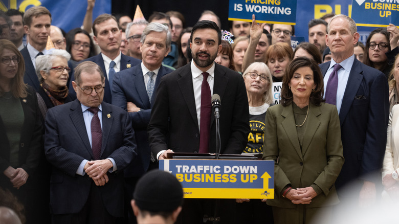 New York Mayor Zohran Mamdani behind a podium with Kathy Hocul to his side, surrounded by people.