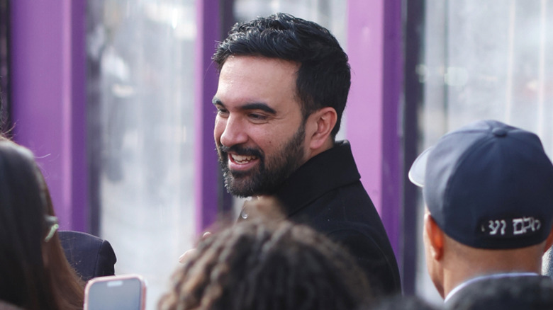Zohran Mamdani smiling above the heads of people surrounding him.