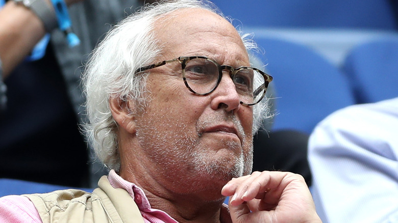 Close up of Chevy Chase with gray hair wearing glasses in a pink shirt