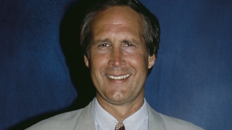 Chevy Chase in light suit and striped tie smiling with hands in pockets