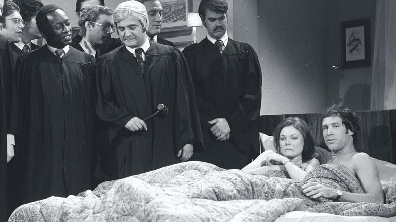 Chevy Chase and Jane Curtin in bed on a SNL skit surrounded by cast dressed as judges