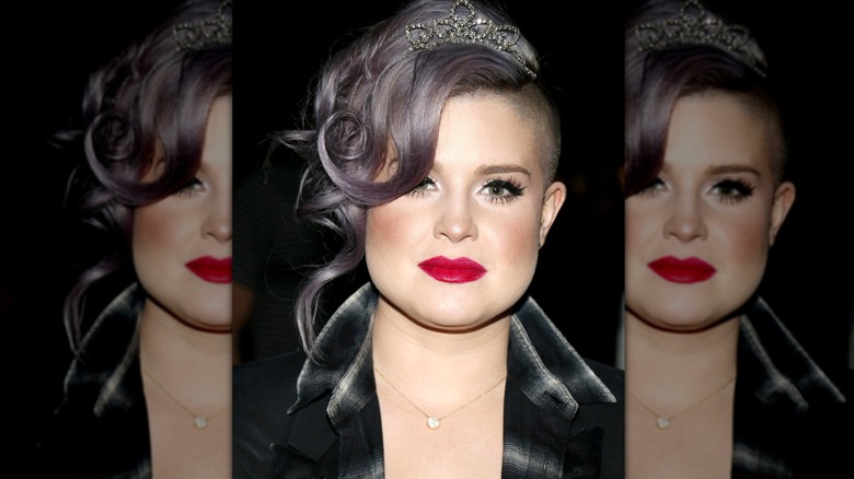 Kelly Osbourne in black jacket with gray hair, red lips, and a tiara