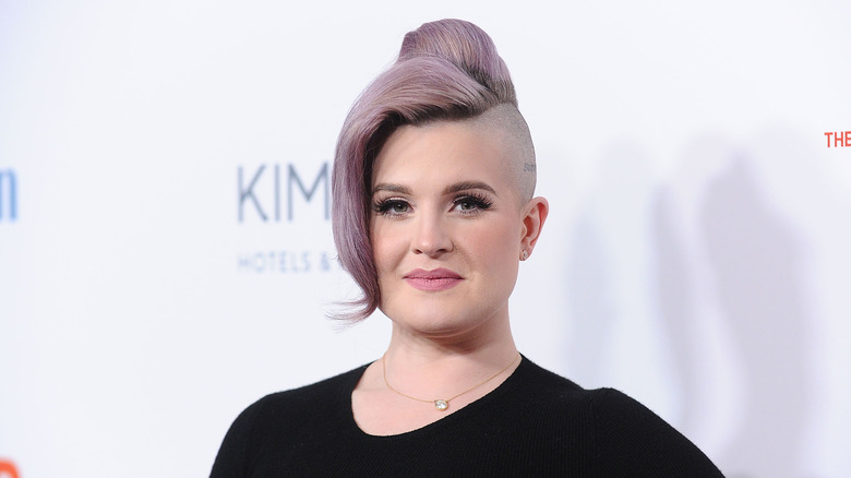 Kelly Osbourne wearing black shirt with purple updo, partially shaved head