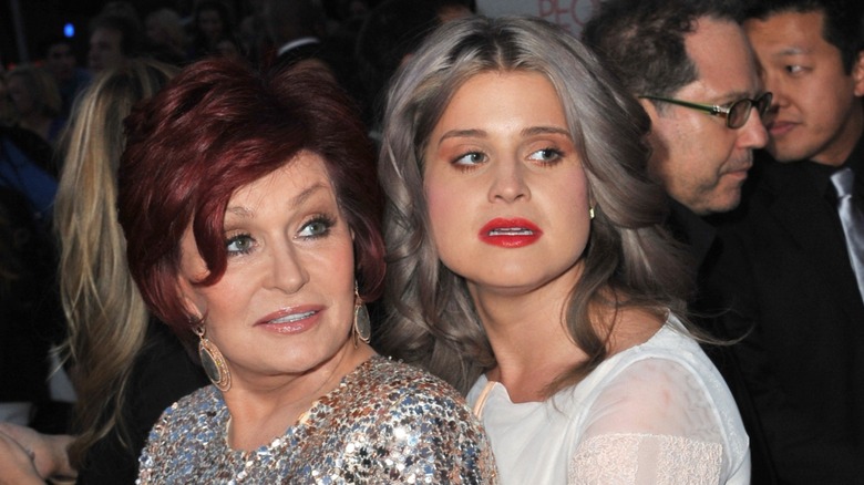 Sharon Osbourne with red hair in silver sequins and Kelly with gray hair red lips and white shirt