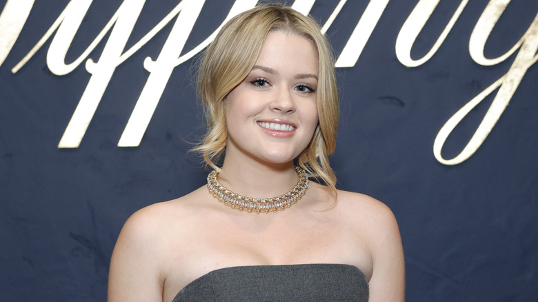 Ava Phillippe in a gray dress, smiling in front of a gray background.