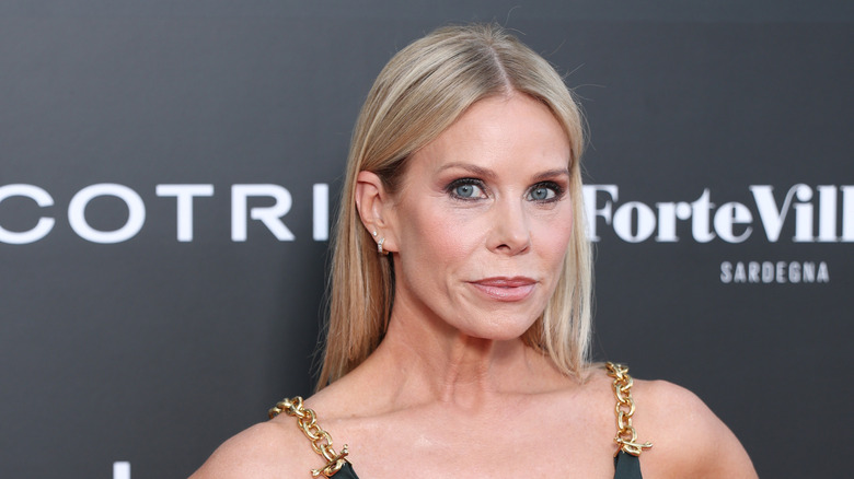 Cheryl Hines posing on the red carpet in a black dress with gold straps