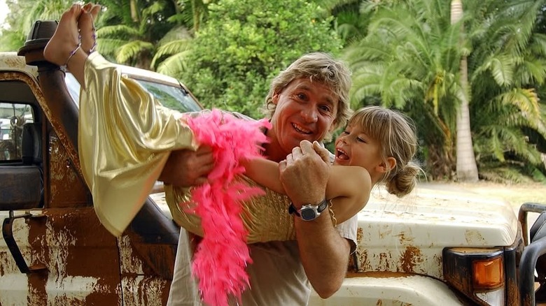 Steve Irwin carries his daughter Bindi Irwin while posing for a photo in front of a truck in the 2000s (2000s)