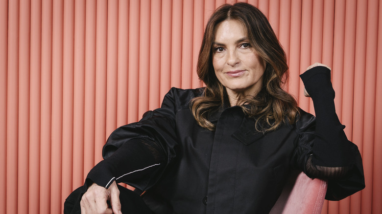 Mariska Hargitay posing in a black jacket in front of a salmon pink background