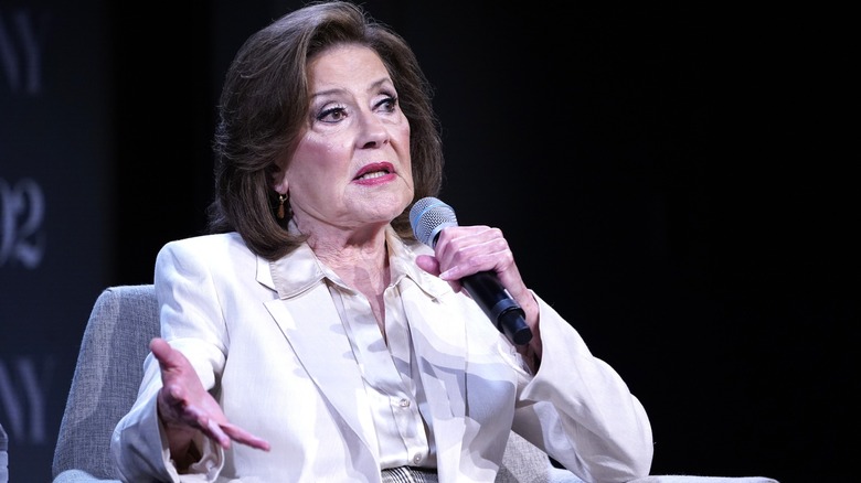 Kelly Bishop in a white suit holding a microphone