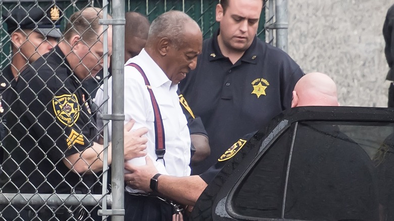 Bill Cosby in handcuffs being loaded into a car