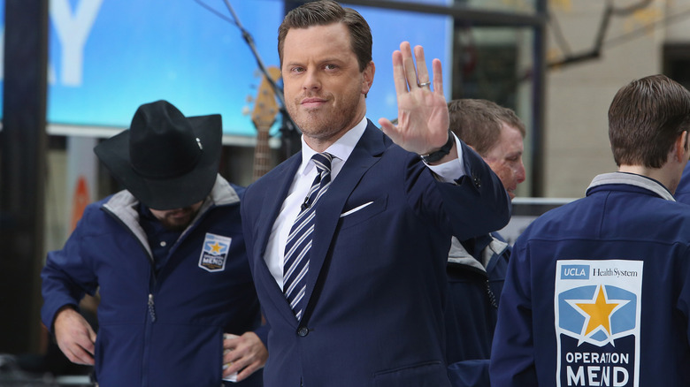 Willie Geist waving at someone, standing among Operation Mend workers