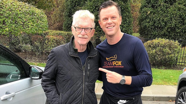 Willie Geist and his dad Bill Geist standing close together outside, with Willie pointing to his dad