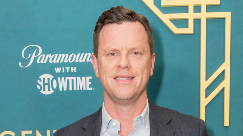 Willie Geist on a red carpet with a teal background, smiling while looking at the camera