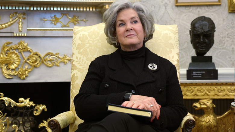 Susie Wiles sitting in the Oval Office in a black outfit with a book in her lap