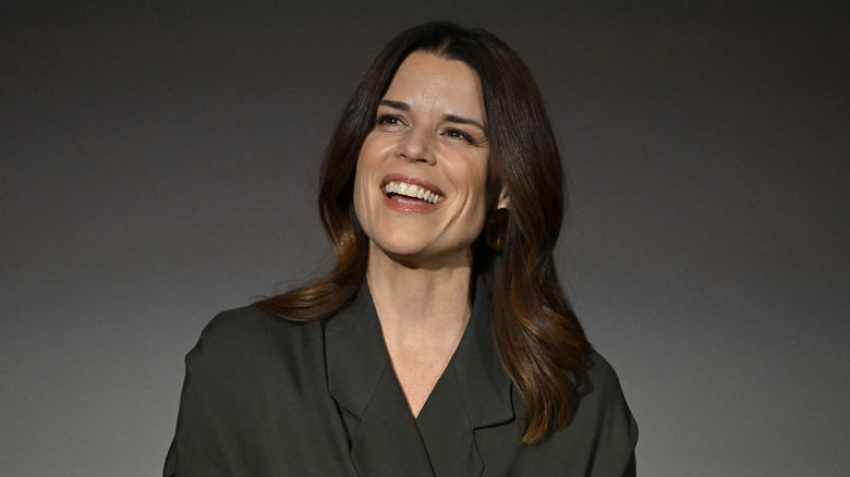 Neve Campbell smiling against a gray background in 2026