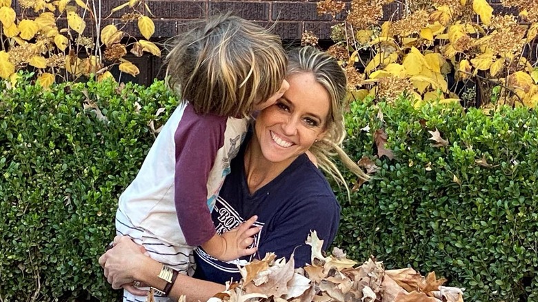 Nicole Curtis smiling and holding her son who's kissing her head outside surrounded by autumn leaves