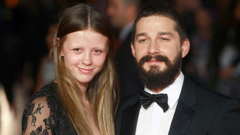 Mia Goth and Shia LaBeouf smile and pose together on the red carpet in black tie attire