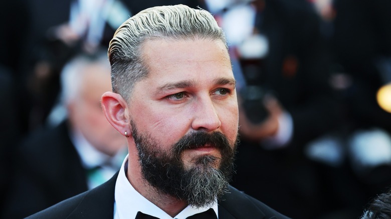 Shia LaBeouf walks the red carpet in 2024 in tuxedo, with slicked back hair, beard, and ear piercing