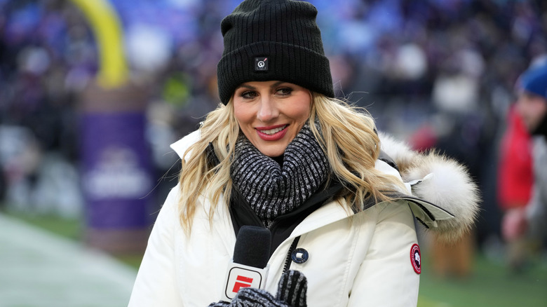 Laura Rutledge smiling in puffer coat and beanie hat while holding ESPN mic