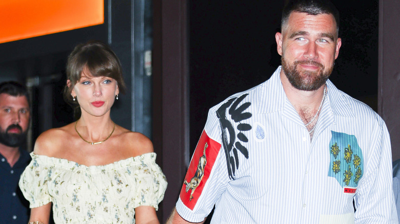 Taylor Swift and Travis Kelce smiling and holding hands