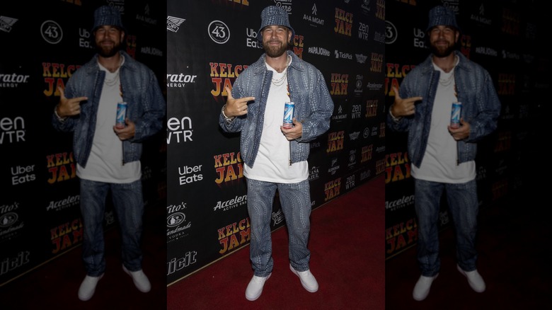 Travis Kelce poses on a red carpet with a drink in hand.