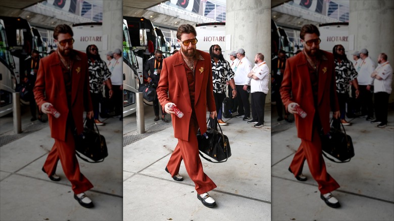 Travis Kelce walking on the sidewalk in a red suit.