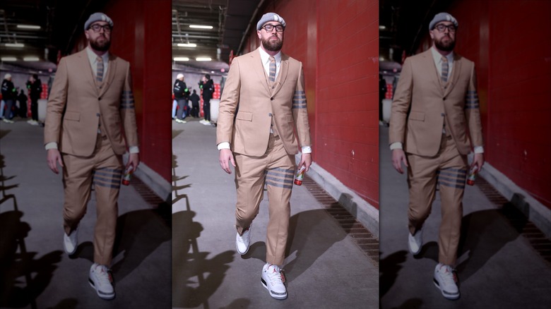 Travis Kelce walks in Cheifs' tunnel in tan suit and hat.