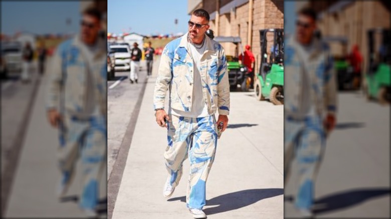 Travis Kelce walks, looking off to the side, in a white and blue outfit.