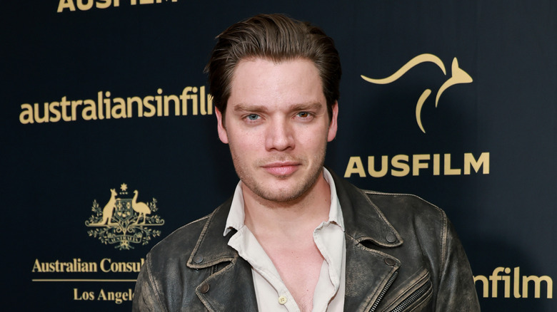 Dominic Sherwood in a white button-down shirt and leather jacket