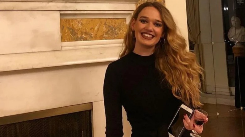 Tricia McLaughlin smiling while holding her phone and a glass of wine in one hand.