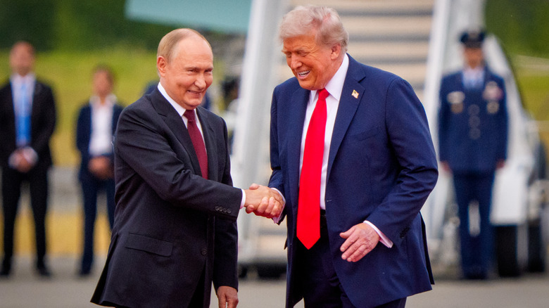 Donald Trump and Vladimir Putin smiling and shaking hands in suits