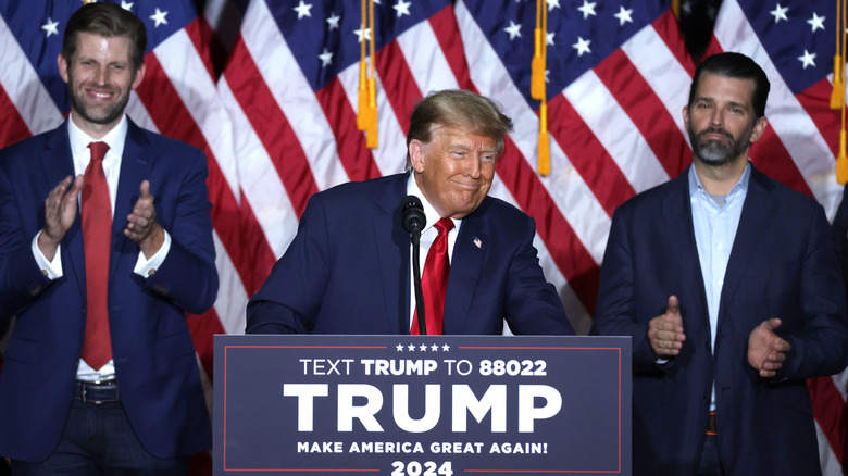 Donald Trump standing behind a podium, flanked by Eric Trump and Donald Trump Jr.