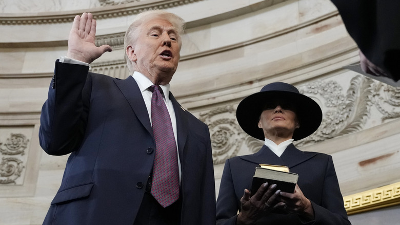 Donald Trump holding his hand up beside Melania Trump at his 2025 inauguration