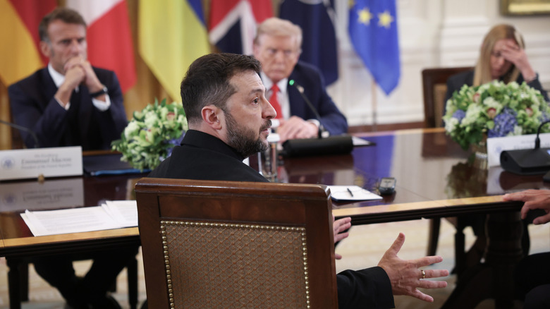 Volodymyr Zelenskyy speaking at a White House meeting while Emmanuel Macron and Donald Trump listen
