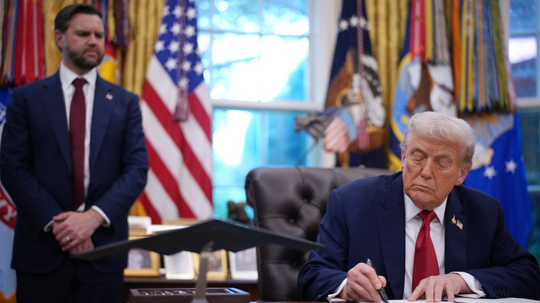 Donald Trump signing paperwork with JD Vance looking on in the background