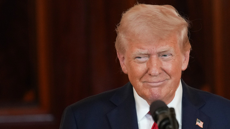 President Donald Trump smiling to himself in front of a microphone