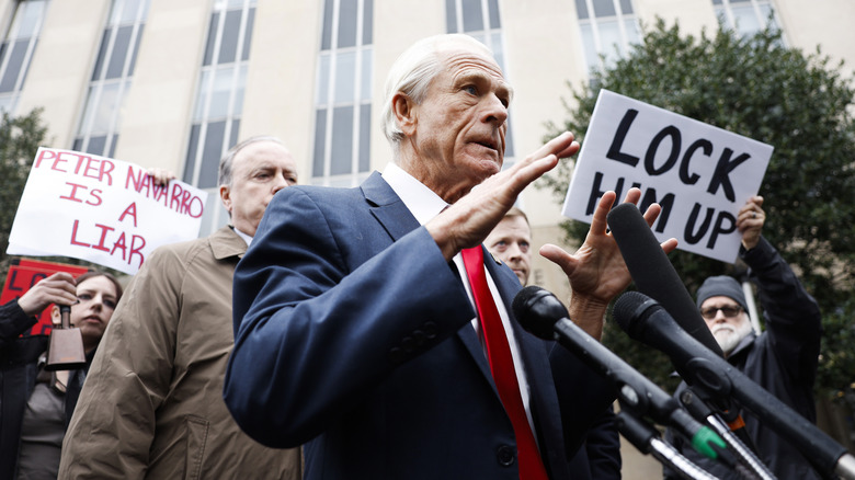 Peter Navarro talking to media on the sidewalk as activists surround him