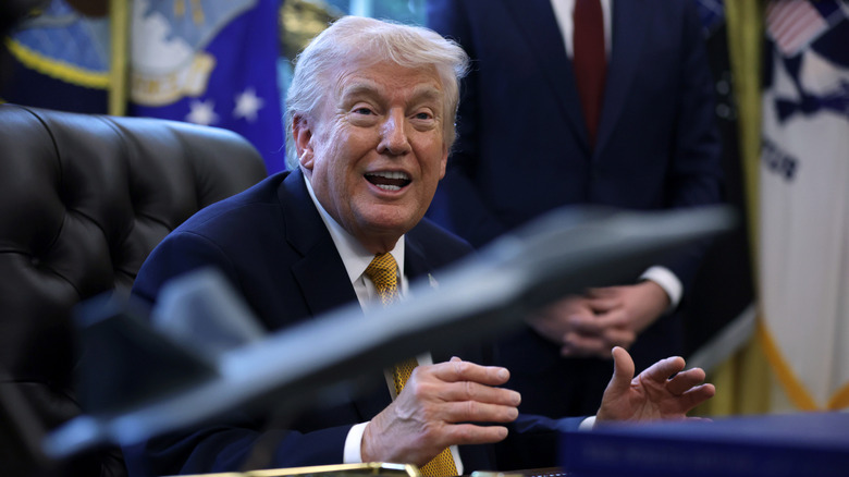 Donald Trump smiling sitting at his desk in the Oval Office