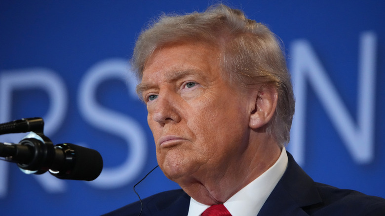 Donald Trump stands in front of a microphone frowning