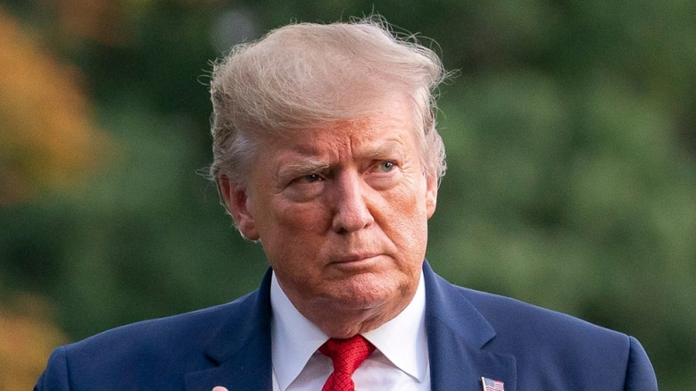 Donald Trump wearing a blue blazer and red tie while waving.