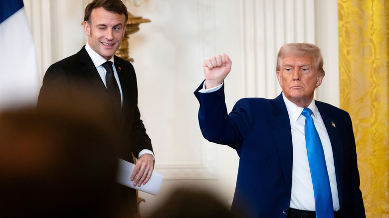 Emmanuel Macron winking while walking next to Donald Trump, who has his fist raised