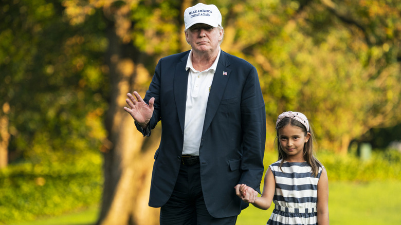 Donald Trump holds Arabella Kushner's hand while waving in a white MAGA hat