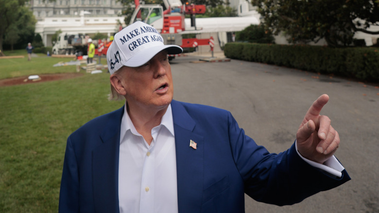 Donald Trump wears a white MAGA hat and points