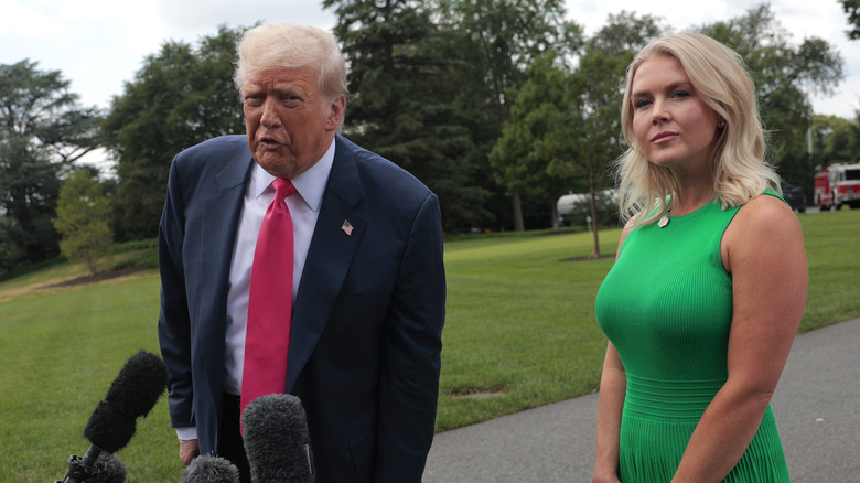 Karoline Leavitt standing behind Donald Trump as he answers press questions at the White House