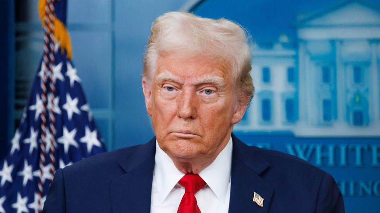 Donald Trump posing while speaking at a White House press briefing in a red tie and a suit.
