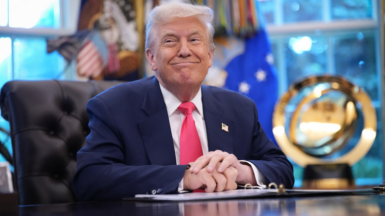 Donald Trump smiling from behind the Resolute desk in the Oval Office