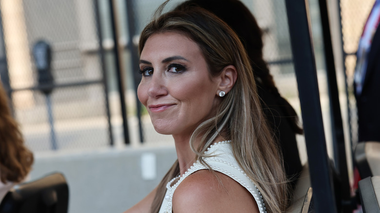 Alina Habba smiling while looking over her shoulder in a white dress