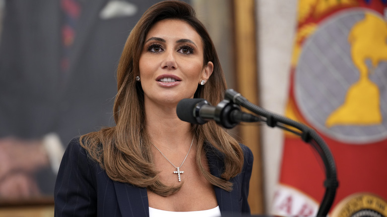Alina Habba speaking in front of a microphone in a navy suit
