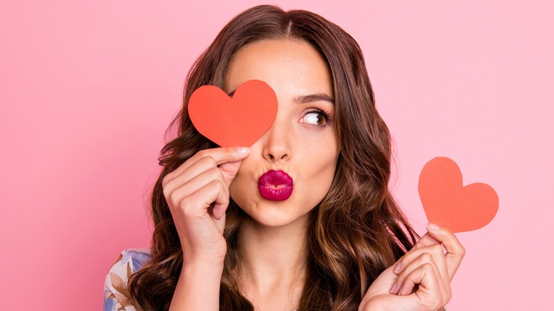 Woman pouts lips holding cutout hearts