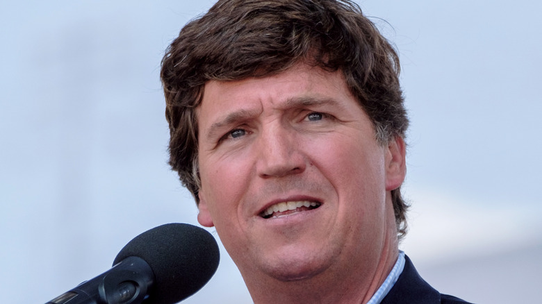 Tucker Carlson in a blue suit in front of a mic